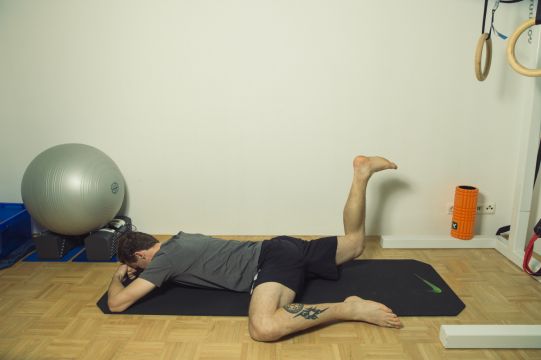 In Bauchlage ein Bein zur Seite und ein Bein nach oben abwinkeln. Anschließend versuchen das Knie des nach oben gewinkelten Beins vom Boden zu heben, bis sich die Gesäßmuskulatur anspannt. 8-10 Wiederholungen pro Seite. Gesäßmuskulatur aktivieren 3